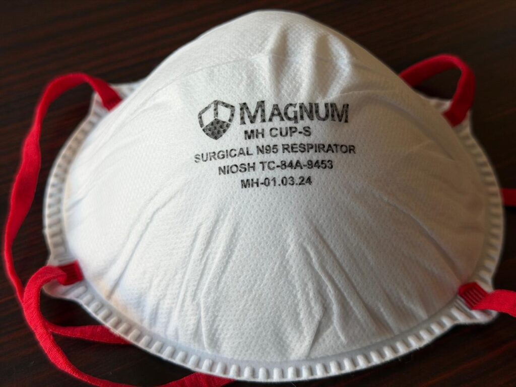 A Magnum MH CUP-S surgical N95 respirator mask with red head straps and NIOSH approval markings