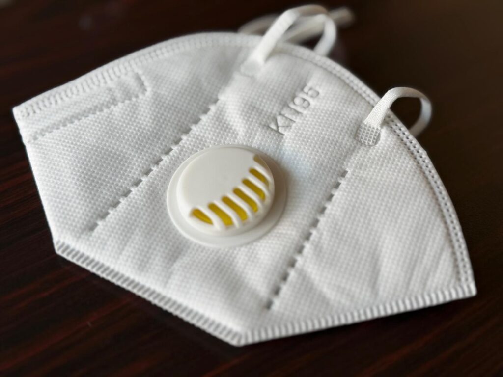 A white KN95 particulate respirator mask featuring an integrated plastic exhalation valve and elastic ear loops