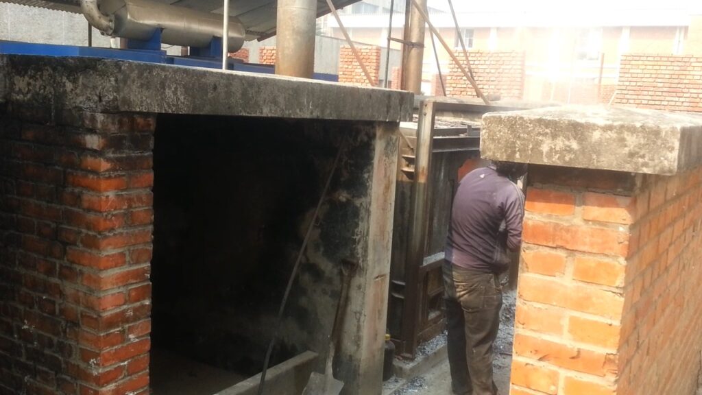 A worker manages waste disposal at a small-scale incineration plant between red brick structures