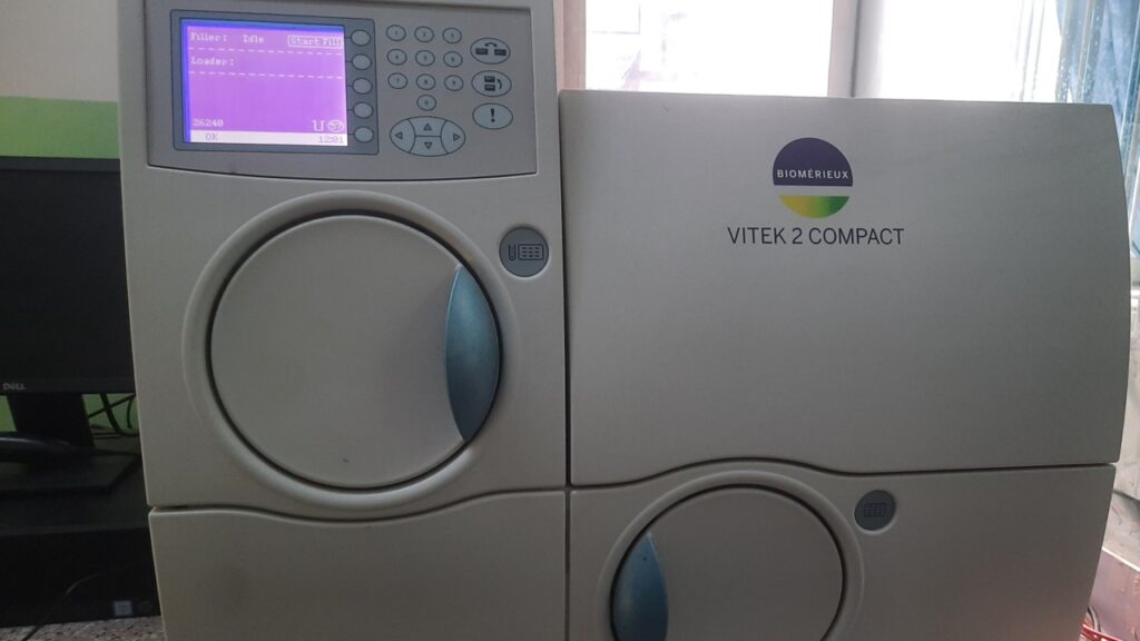 The image shows a front view of the bioMérieux VITEK 2 Compact, a benchtop automated system designed for rapid microbial identification and antibiotic susceptibility testing in clinical laboratorie